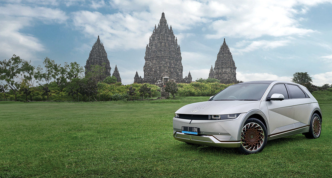 Hyundai Ioniq 5 berwarna putih terparkir di atas rumput hijau dengan latar belakang megahnya Candi Prambanan.